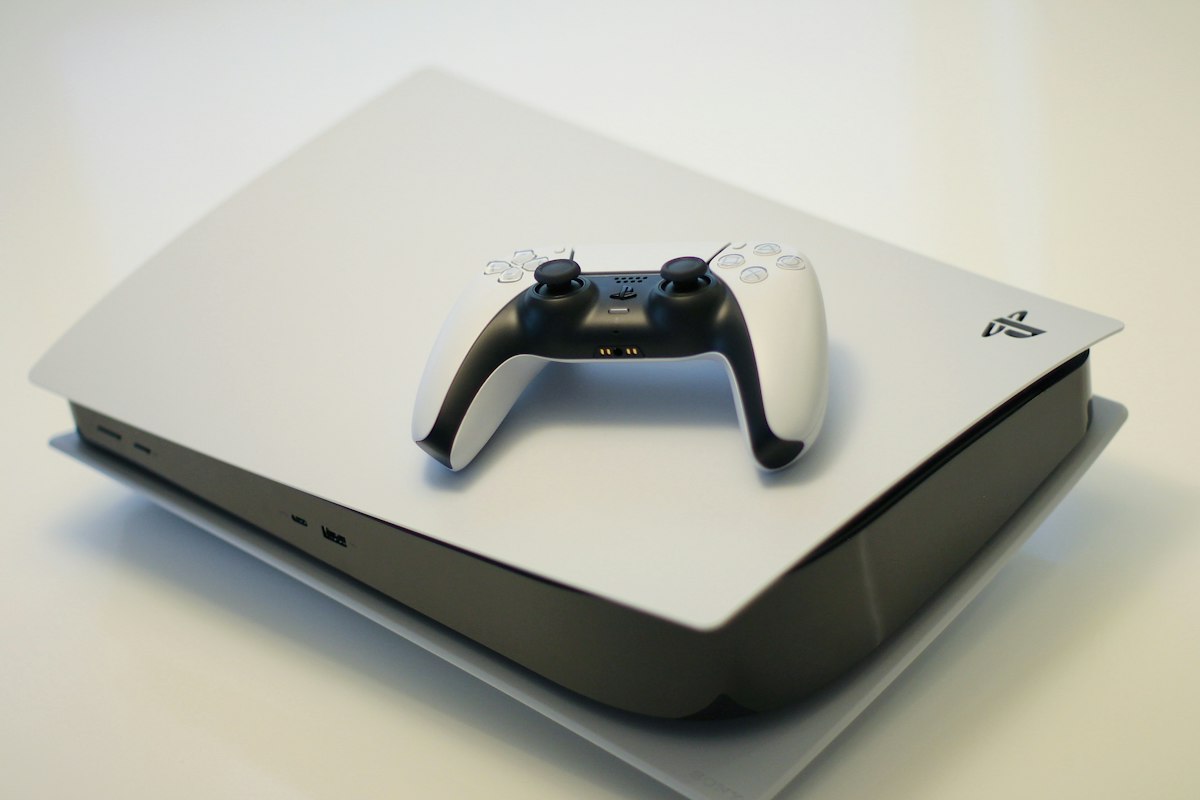 A PlayStation 5 console with a DualSense controller resting on its white face plate — generic console stock photo illustrating the PS5-porting section below, not a photo of AnyPS5 or any software it produces